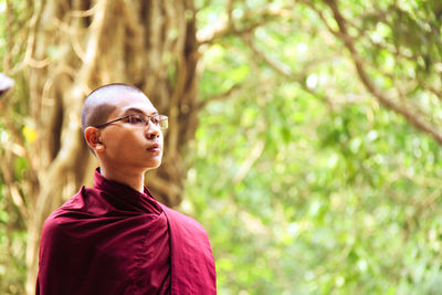 Young monk looking away against trees