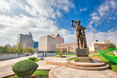 Statue by buildings against sky in city