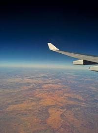 Airplane wing over landscape against clear blue sky