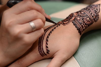 Cropped hand of woman applying henna tattoo of friend hand