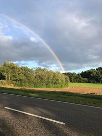 Rainbow over road against sky