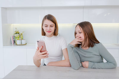 Young woman using mobile phone while sitting on hardwood floor at home