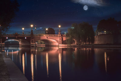 Illuminated bridge over river in city against sky at night