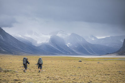 Rear view of people walking on field against mountains