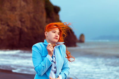 Young woman standing at beach against sky