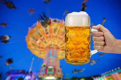 Close-up of hand holding beer glass against blue background