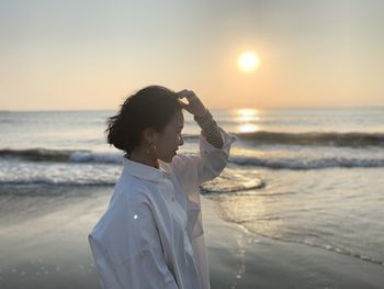 Woman standing at beach against sky during sunset