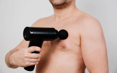 Midsection of shirtless man using percussion massager
