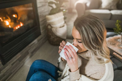 High angle view of woman drinking coffee while sitting by fireplace