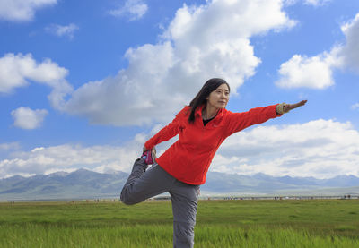 Young woman exercising on grassy landscape against sky