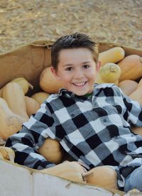 Portrait of happy boy sitting in box with pumpkins