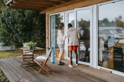 Rear view of man opening door for woman while standing on porch outside house