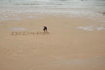 Rear view of man writing on sand at beach