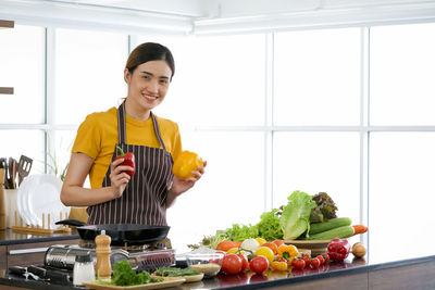 Smiling young woman standing by fruits in kitchen