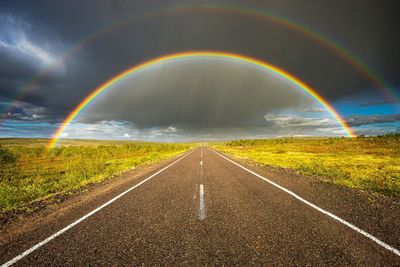 Rainbow over road against sky