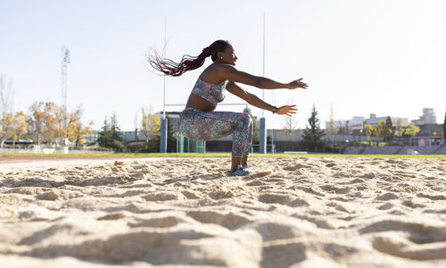 Female sportsperson balancing on sand against clear sky during sunny day