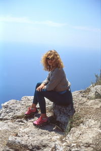 Woman sitting on rock against sky