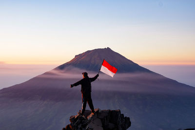 Rear view of man standing on mountain against clear sky during sunset