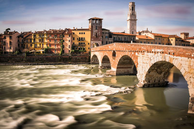 Arch bridge over river against buildings in city