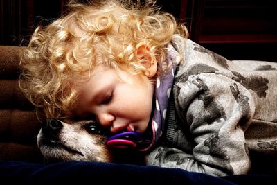 Close-up of toddler girl relaxing with dog on couch