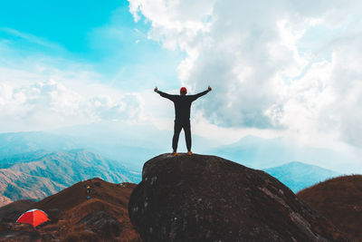 Rear view of man standing on rock against sky