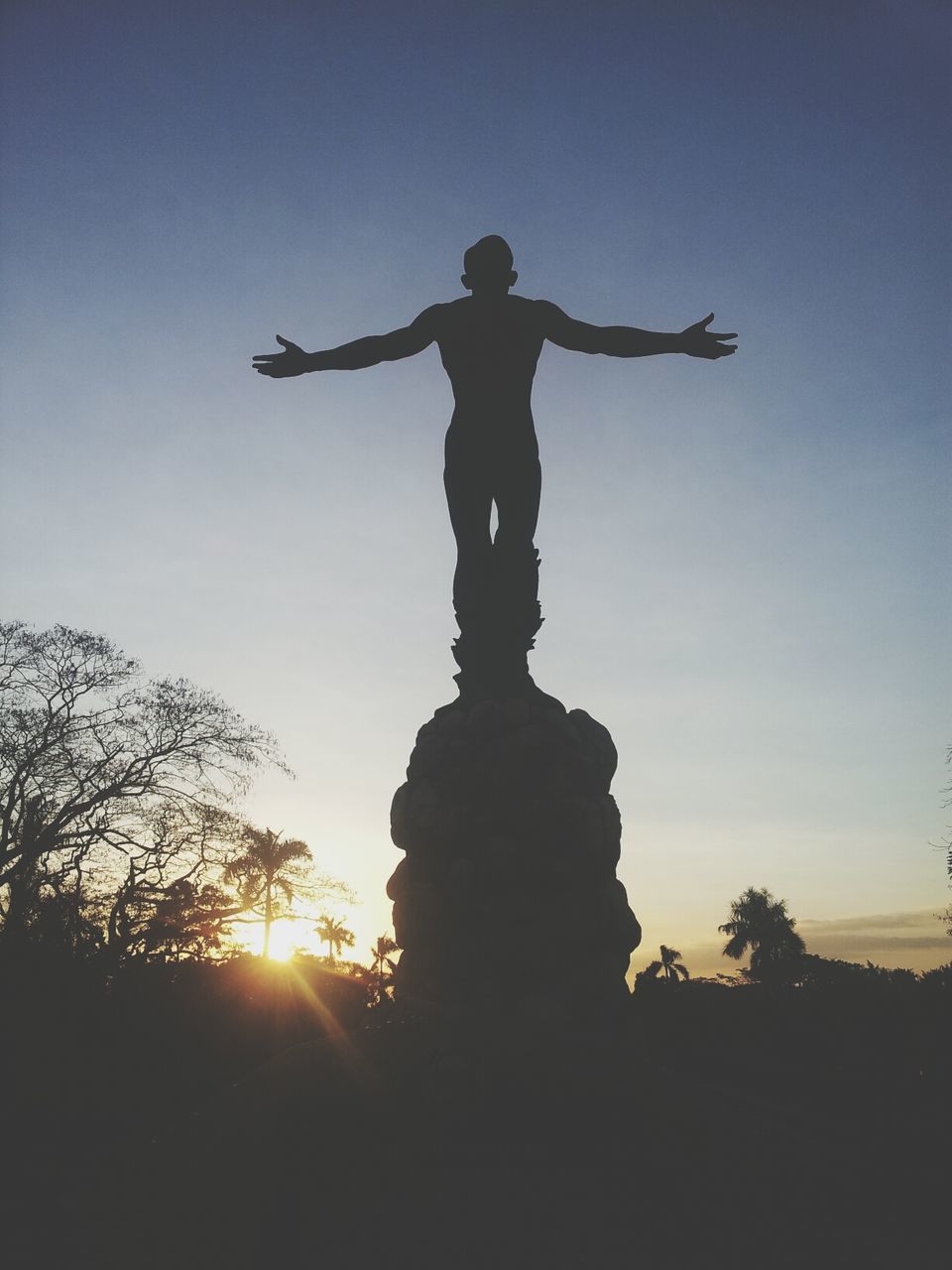 statue, human representation, sculpture, silhouette, art and craft, art, creativity, sunset, low angle view, tree, sun, sky, religion, clear sky, sunlight, spirituality, sunbeam, travel destinations