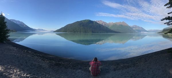 Panoramic view of man sitting by lake against sky