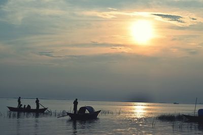 Silhouette people on boat in sea against sky during sunset