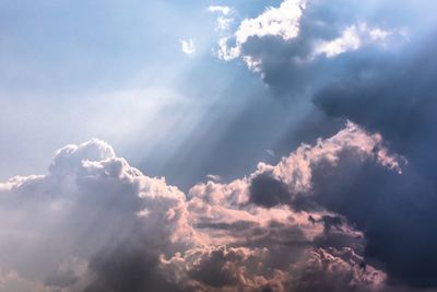 Low angle view of sunlight streaming through clouds