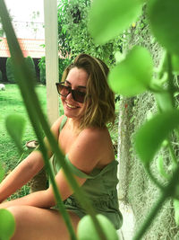 Smiling woman wearing sunglasses sitting by plants