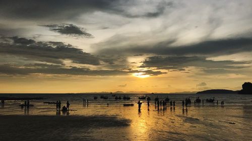 Silhouette people on beach against sky during sunset