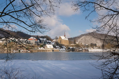 Bare trees by buildings against sky during winter