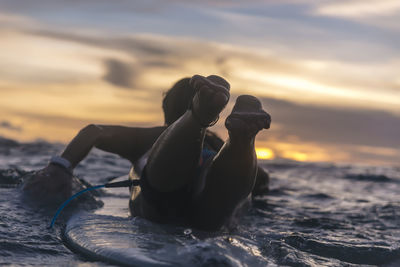 Rear view of young woman lying on surfboard while swimming in sea during sunset