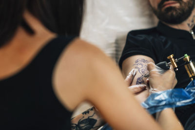 Female tattoo artist tattooing mans arm in studio