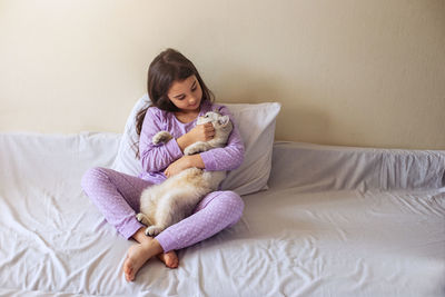 Girl with cat sitting on bed at home