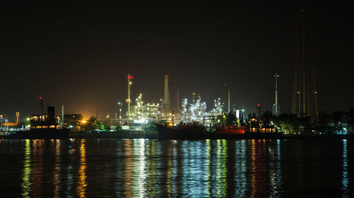 Illuminated factory by river against sky at night