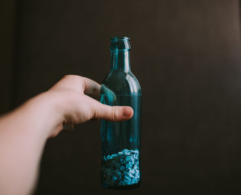 Hand holding glass bottle against black background