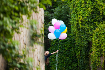 Person holding colorful balloons against trees