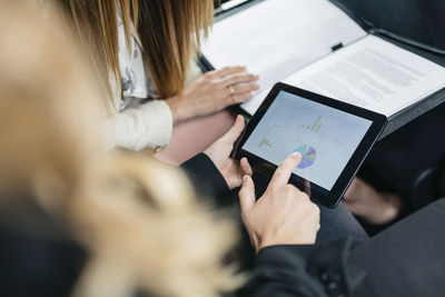 Two businesswomen with digital tablet and documents working in car