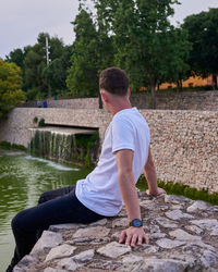 Side view of man sitting on retaining wall