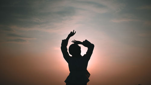 Silhouette woman with arms raised standing against sky during sunset