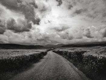 Dirt road amidst field against sky