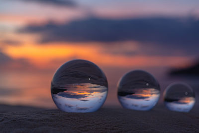 Close-up of crystal ball on beach against sky during sunset