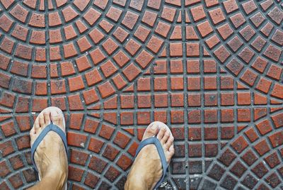 Low section of man wearing flip-flop while standing on footpath