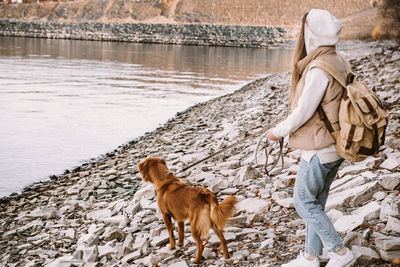 Young woman and dog retriever walks on river shore at autumn season