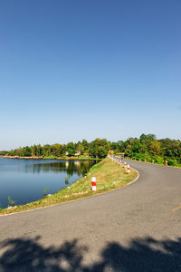 Road by trees against clear blue sky