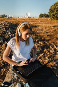 Young woman using laptop sitting on land against sky