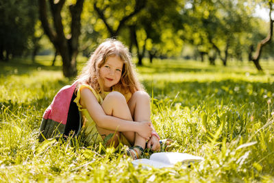 A cute schoolgirl is sitting on the grass in the park and reading a book
