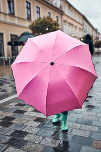 Little girl hiding behind big pink umbrella walking in a downtown on rainy gloomy autumn day