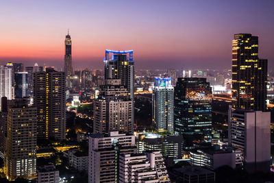 Illuminated modern buildings in city against sky at night